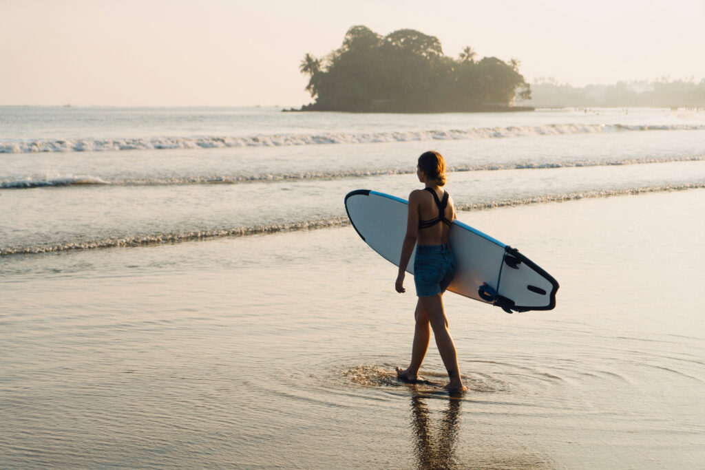 Frau mit Surfbrett am Strand in Sri Lanka