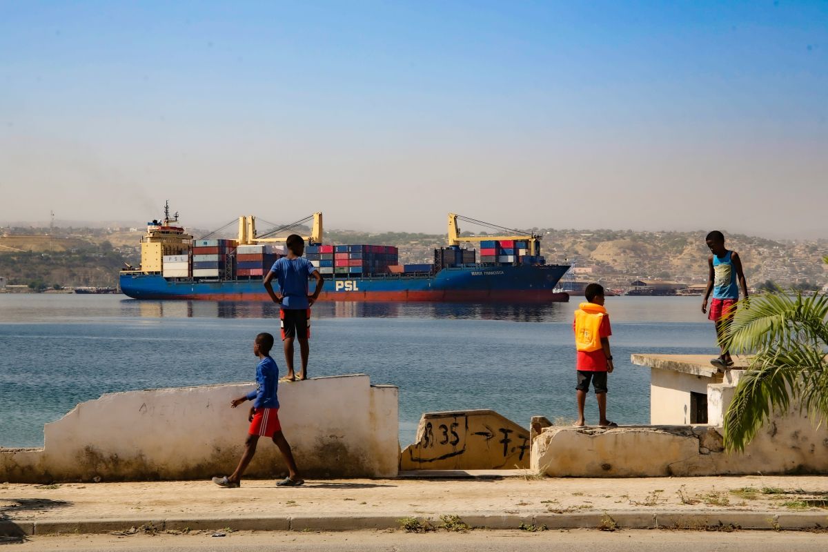 Kinder spielen am malerischen Hafen von Lobito, Angola, mit Blick auf ein beeindruckendes Schiff