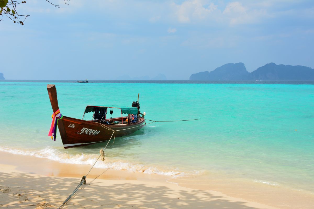 Boot am Strand in Thailand mit türkisblauem Wasser und sanften Wellen