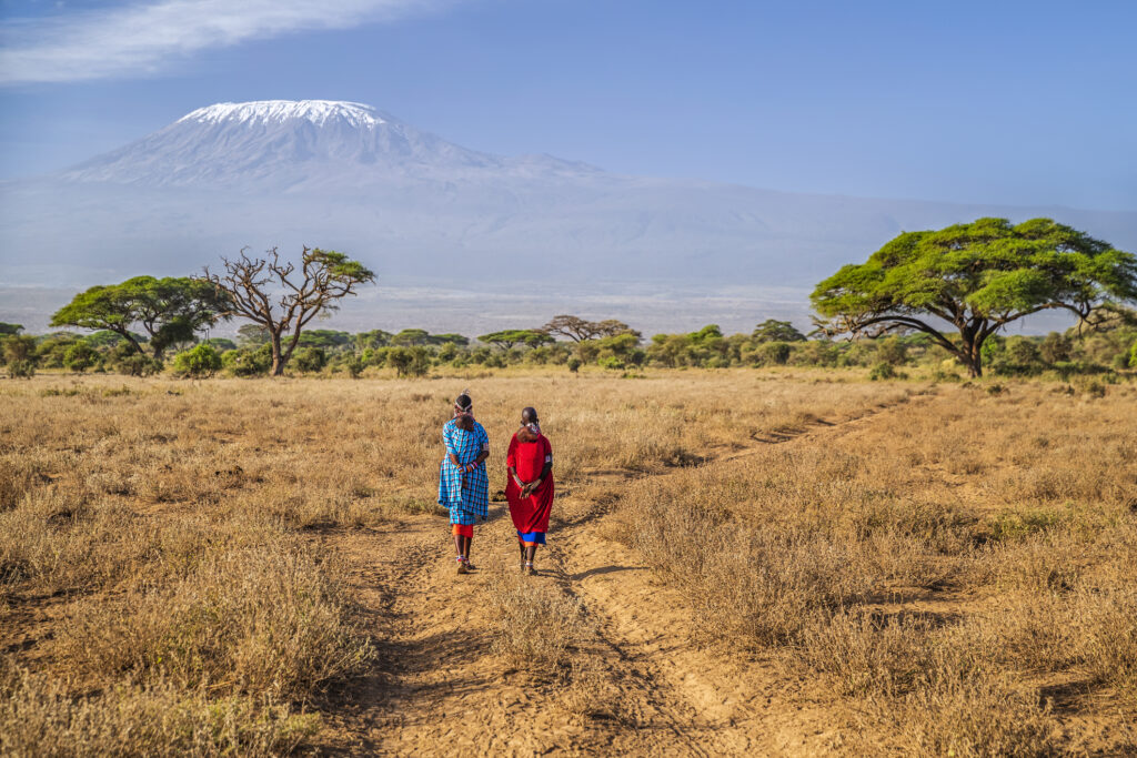 Zwei Frauen aus Kenia von hinten aufgenommen, gehen auf einem Weg in der Afrikanischen Landschaft