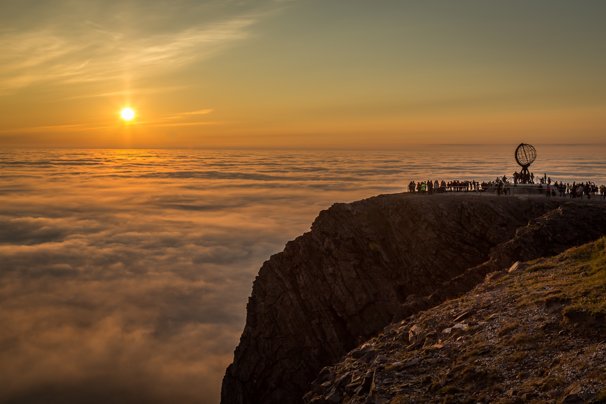Felsen mit Touristen in Norwegen ausblickend auf Mitternachtssonne über Wolken