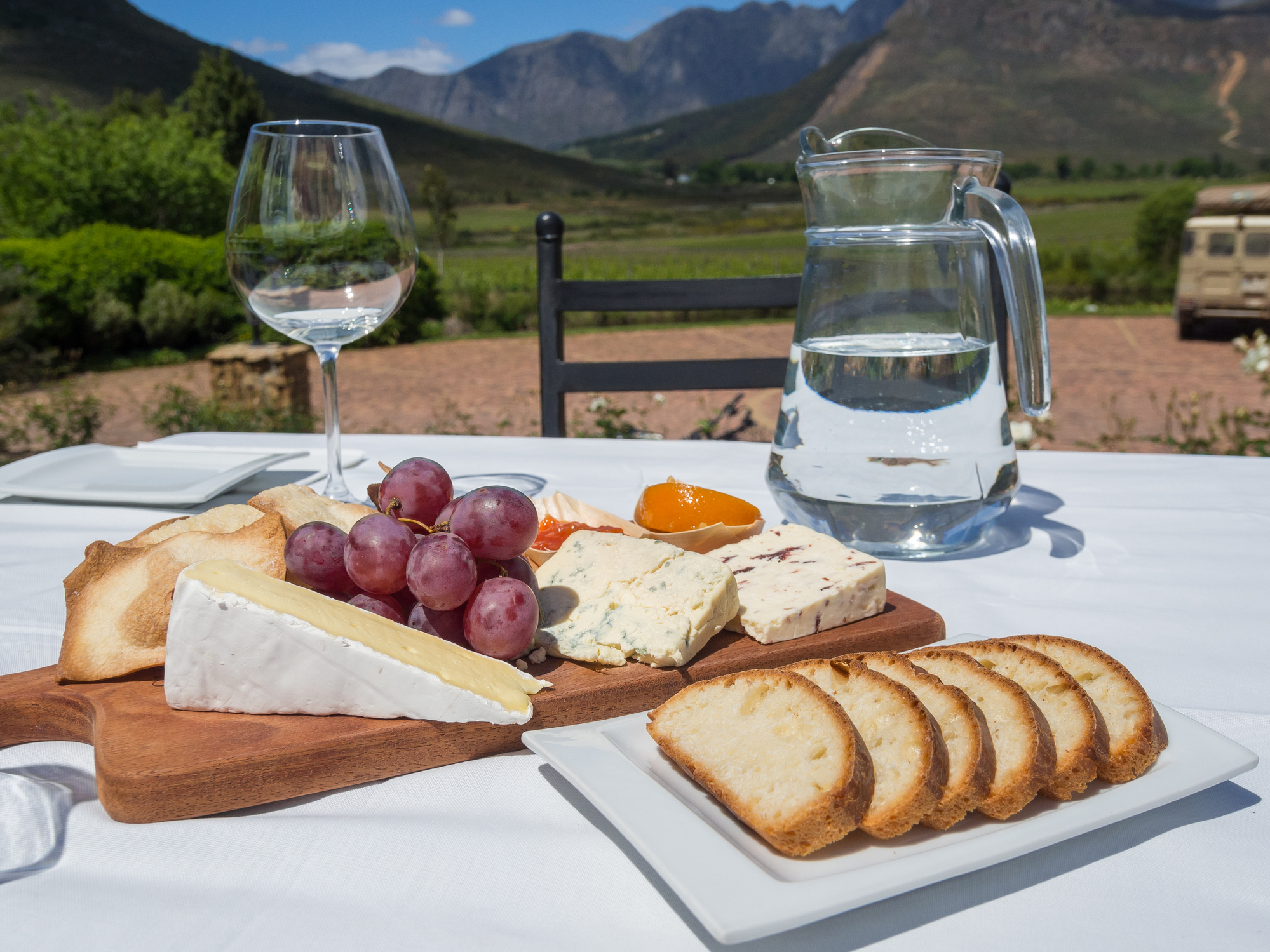 Käseplatte mit Brot, Wasser und Weinklass vor der Landschaft Südafrikas