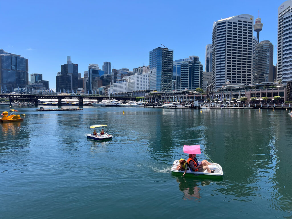 Menschen im Tretboot auf Wasser vor Hochhäusern am Hafen von Sydney