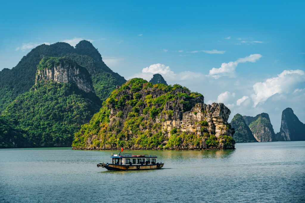 Hanoi Bucht Vietnam mit Felsen die aus dem Ozean ragen und kleinem Boot davor