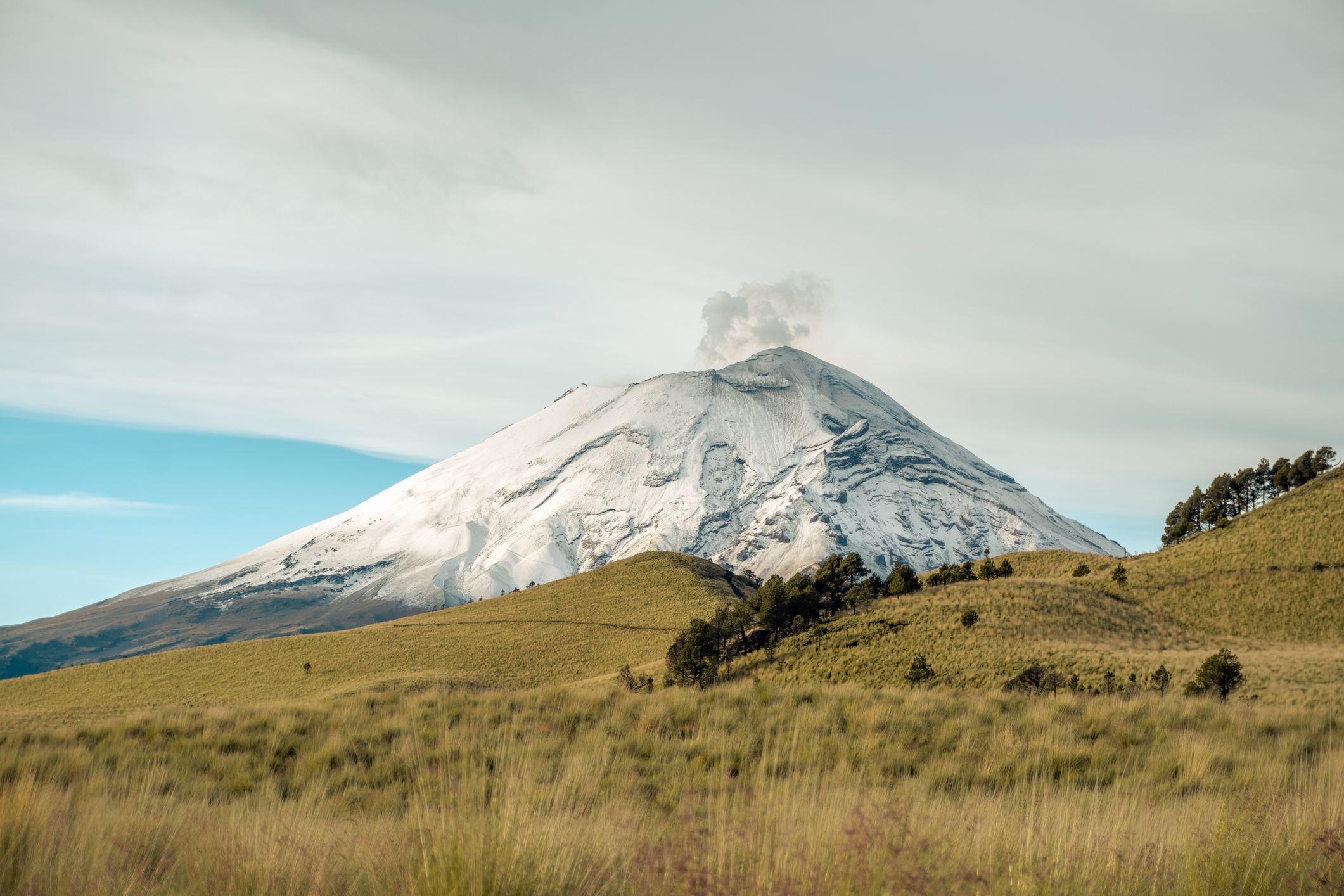 Der aktive Stratovulkan Popocatépetl stößt eine Rauch- und Aschewolke in den Himmel aus, die von den grasbewachsenen Hängen von Iztaccihuatl aus zu sehen ist.