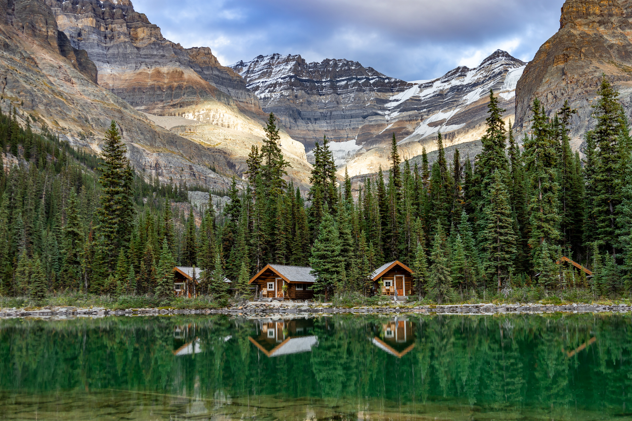 Die Hütten am Lake O'Hara spiegeln sich im smaragdgrünen Wasser des Sees, im Hintergrund erheben sich Berggipfel, Yoho-Nationalpark, Kanada.
