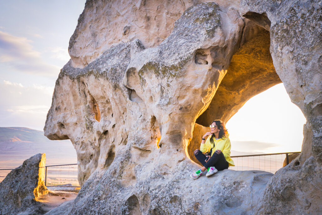 Eine Touristin sitzt auf dem Felsen von Uplistsikhe und genießt den Panoramablick.