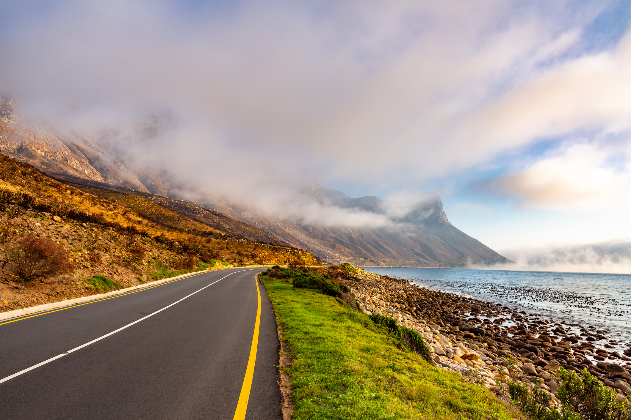 Straße mit Bergen, Wolken und einer Autobahn in der Nähe von Kapstadt, Südafrika.