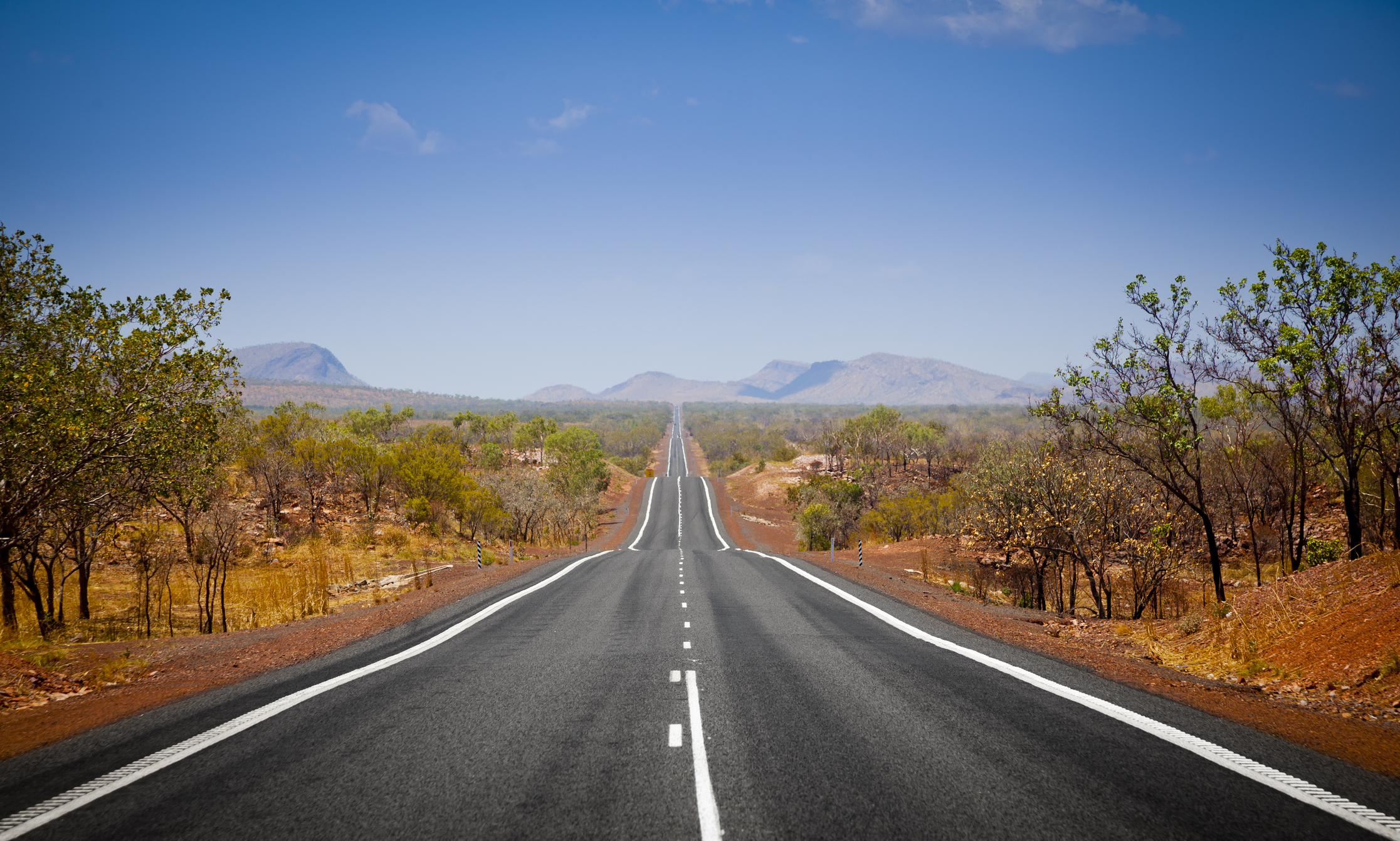 Weite Straße in AUstralien mit roter Erde an den Straßenseiten