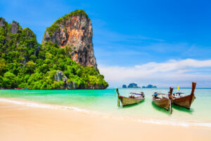 Boote an einem wunderschönen Strand mit Kalksteinklippen und kristallklarem Wasser in Thailand