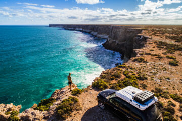Luftaufnahme eines geparkten Autos mit Wohnwagen und eines jungen Mannes, der auf die Große Australische Bucht blickt.