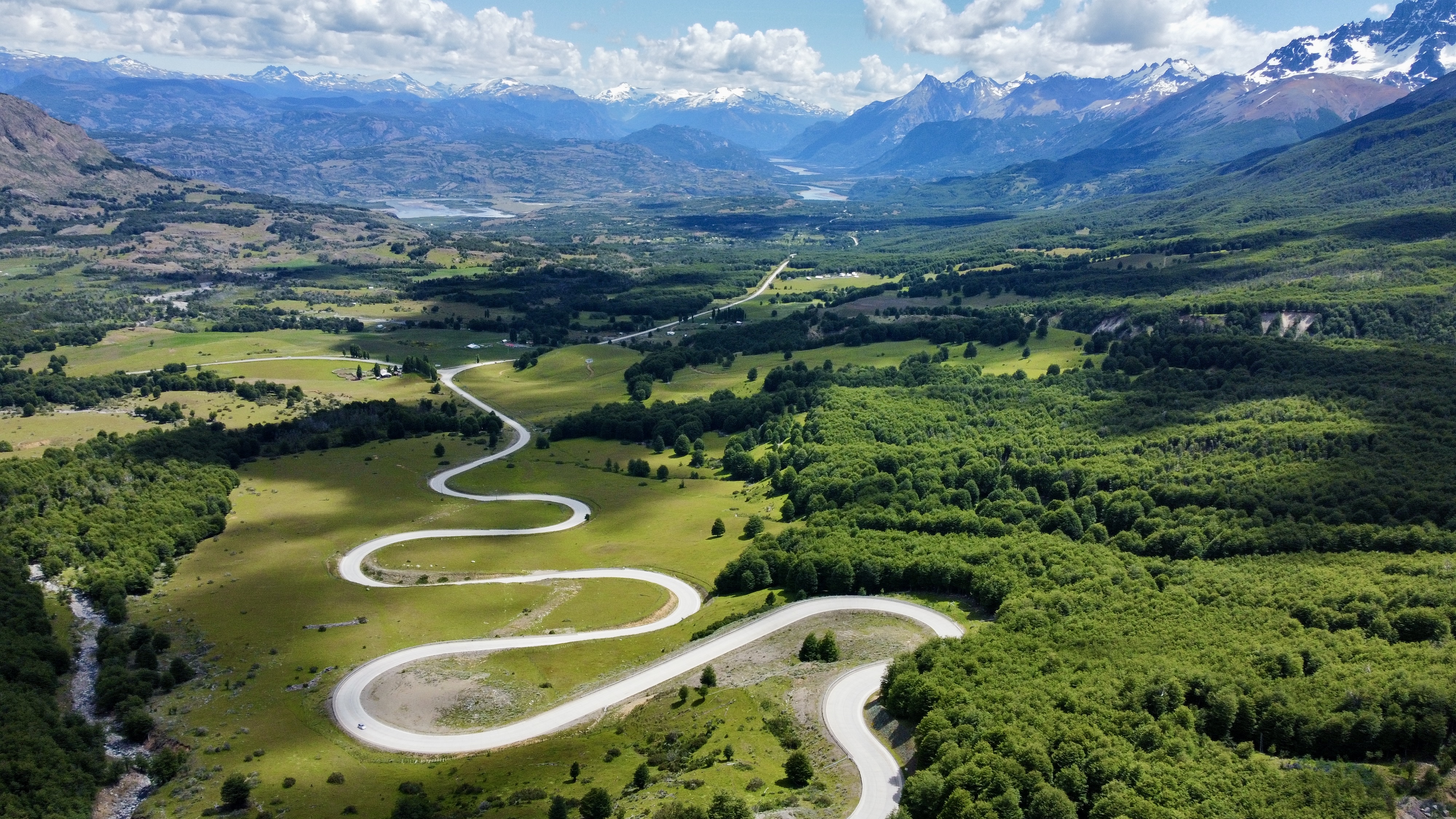 Luftaufnahme einer kurvenreichen Straße der Carretera Austral, die durch grüne Felder und dichte Wälder in der atemberaubenden Region Cerro Castillo im chilenischen Patagonien führt. 