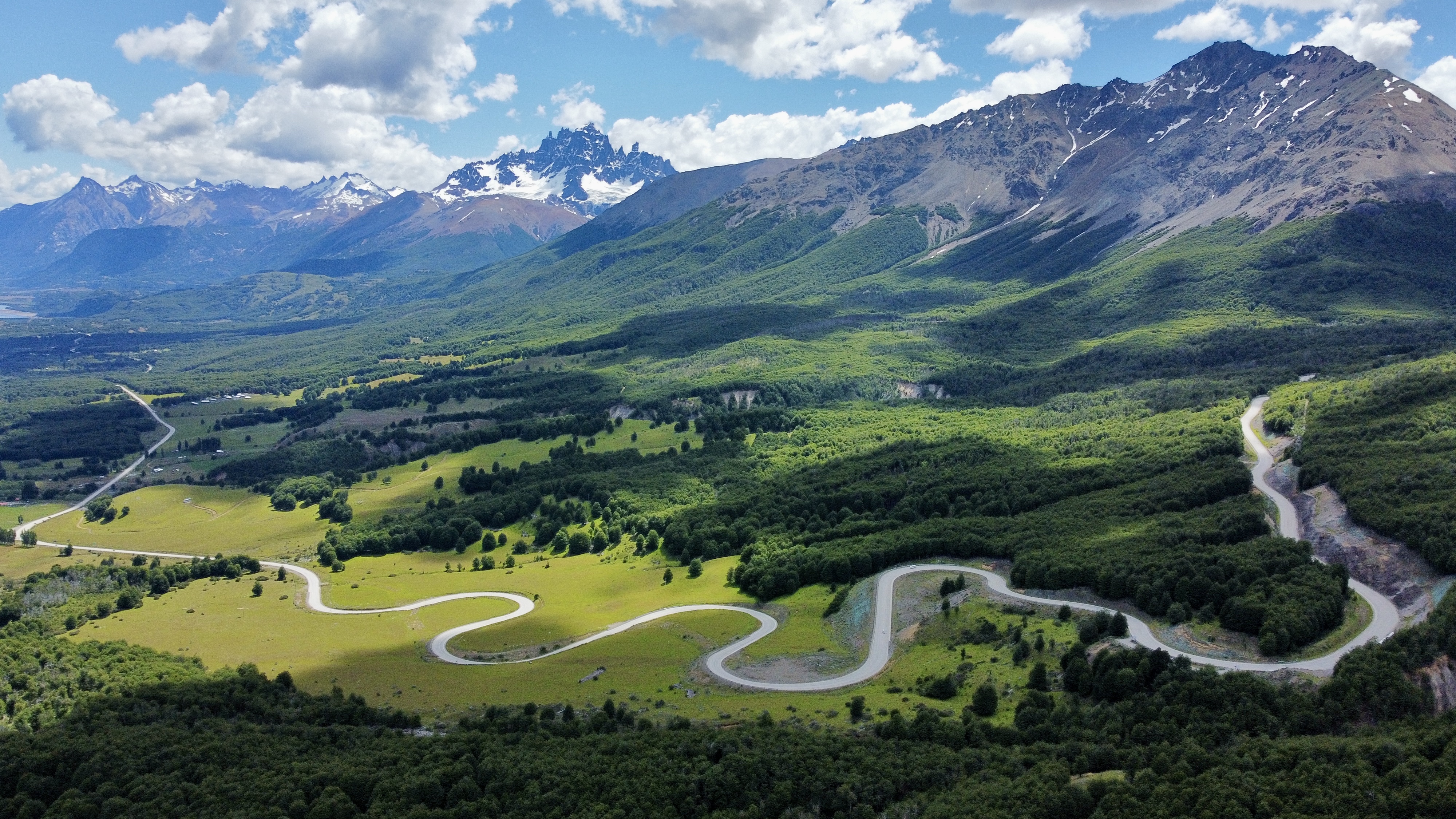 Luftaufnahme der Carretera Austral, die sich durch die üppig grünen Landschaften des chilenischen Patagoniens schlängelt, mit dem majestätischen Cerro Castillo und seinen schneebedeckten Gipfeln als atemberaubender Kulisse.