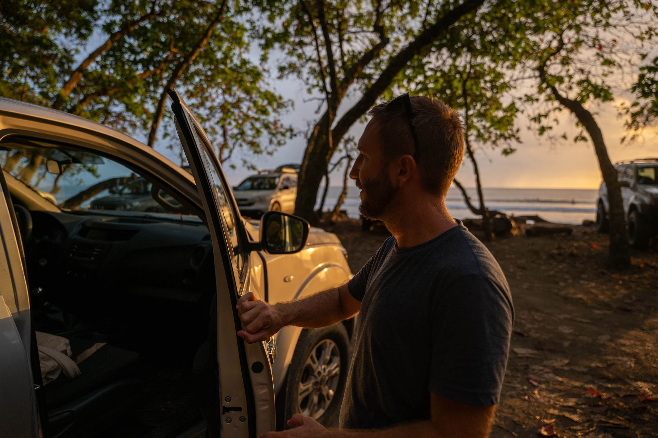 Mann steht neben offener Autotür bei malerischem Sonnenuntergang am Strand