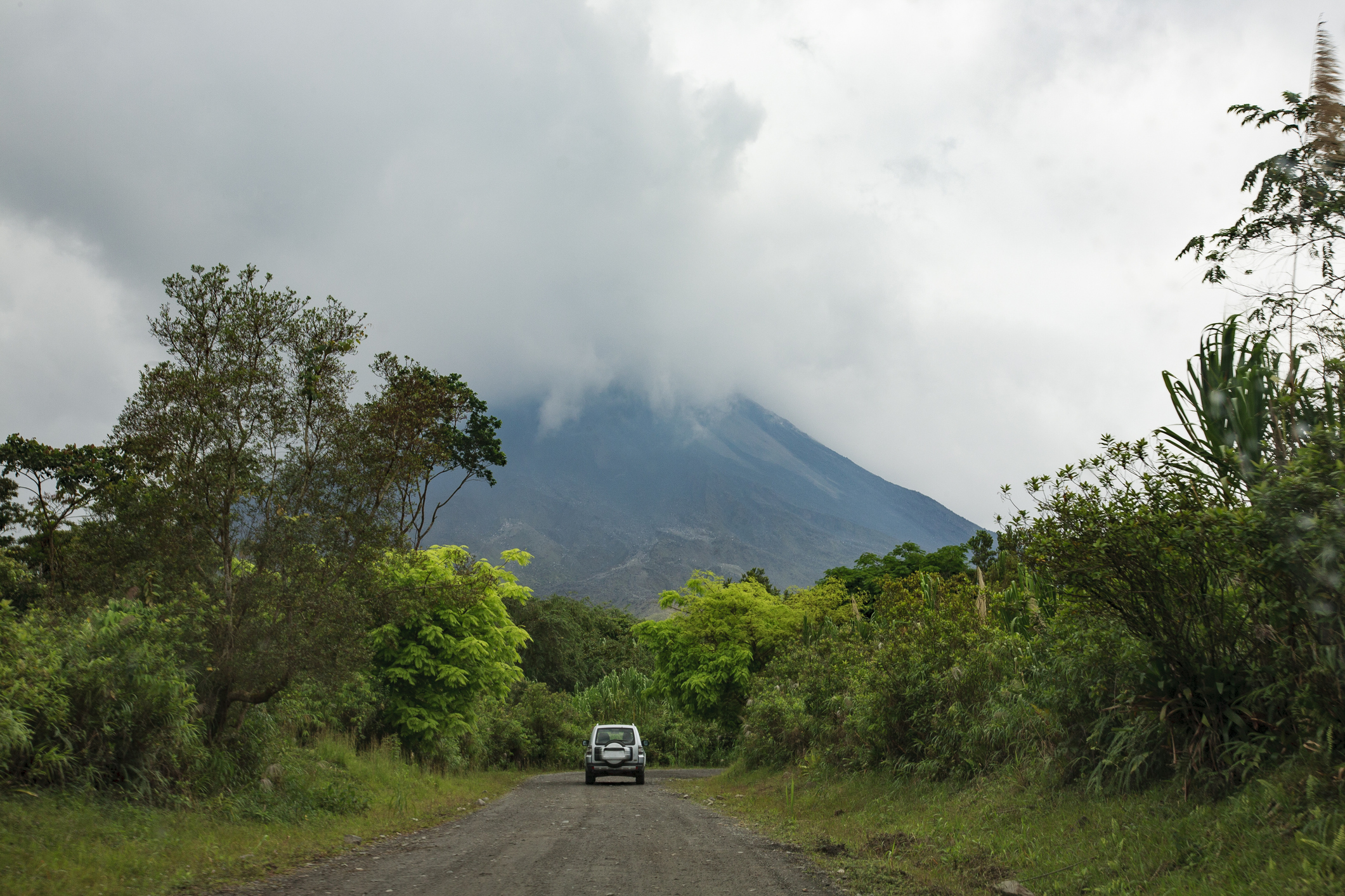 Auto auf Straße mit Vulkan und Wolken im Hintergrund