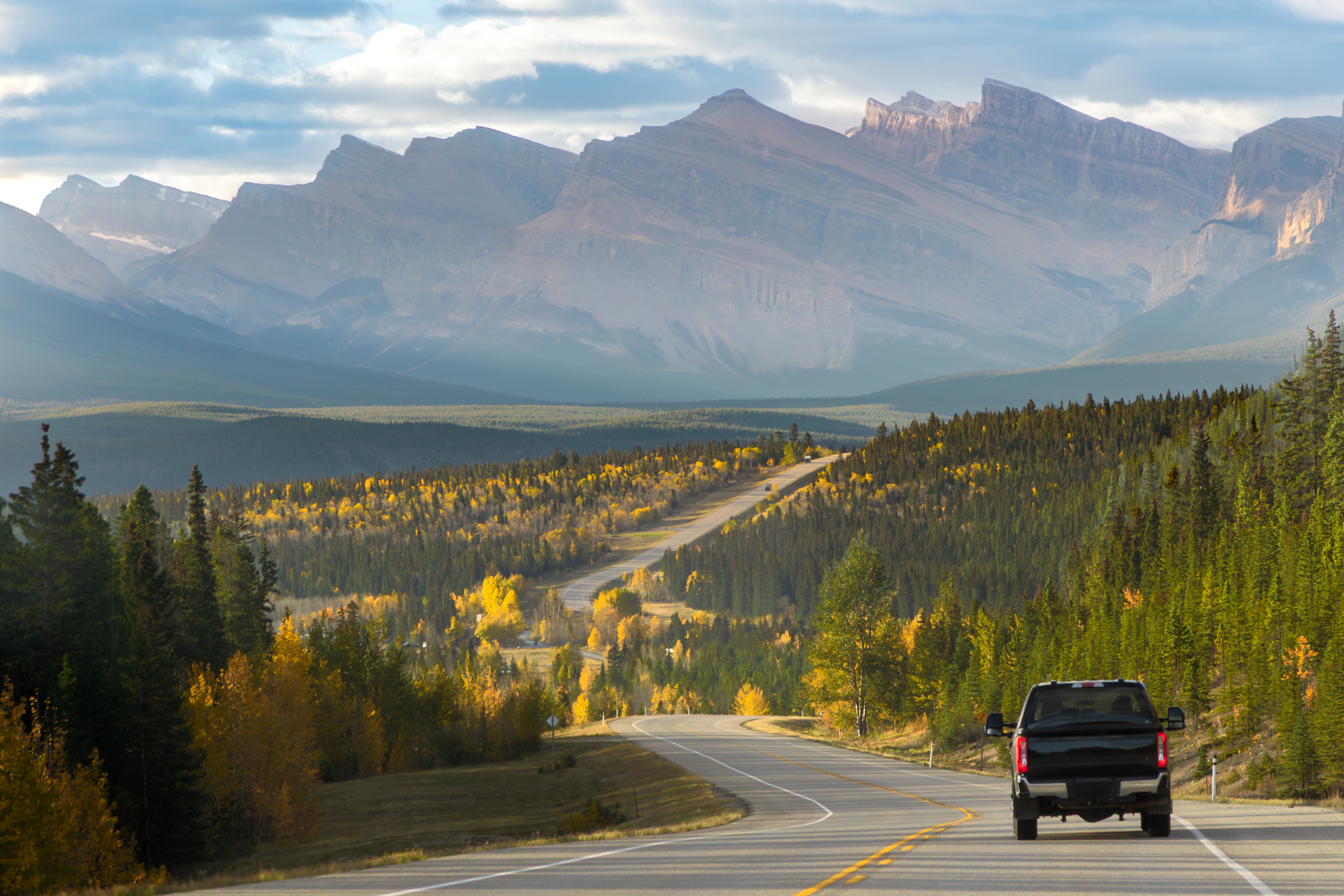 Pickup-Truck fährt auf herbstlicher Straße in Alberta in Richtung Gebirgskette