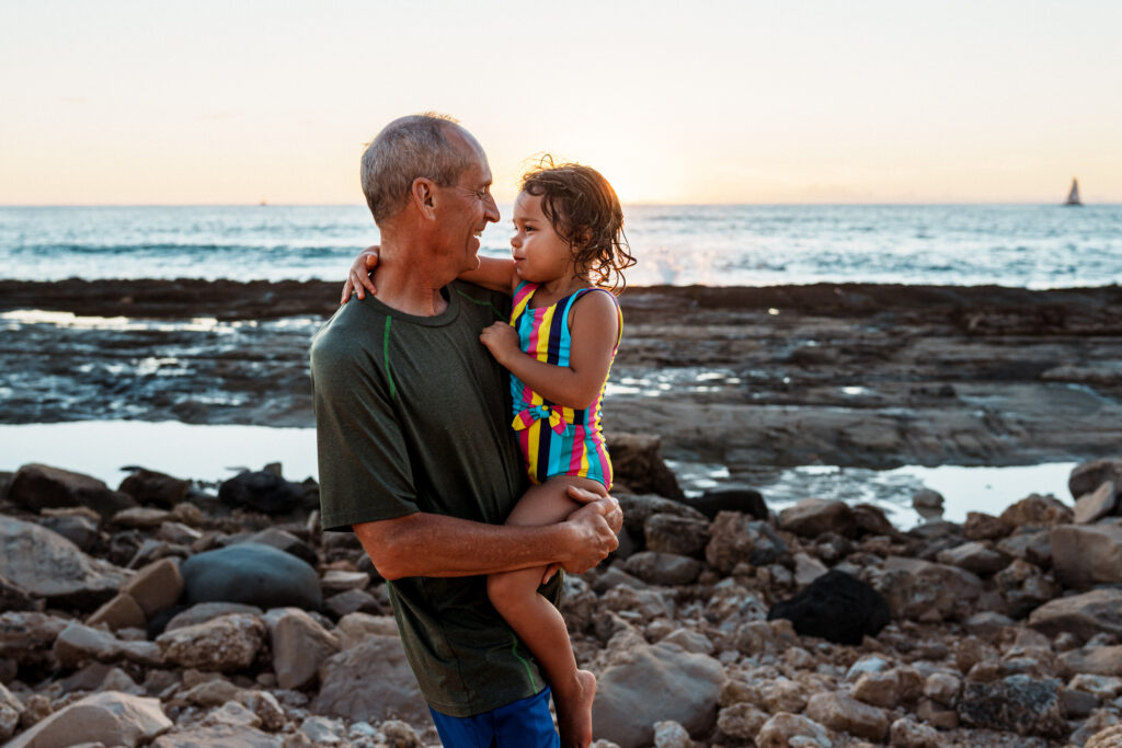 Großvater hält Kleinkind im Arm, während er am felsigen Ufer steht
