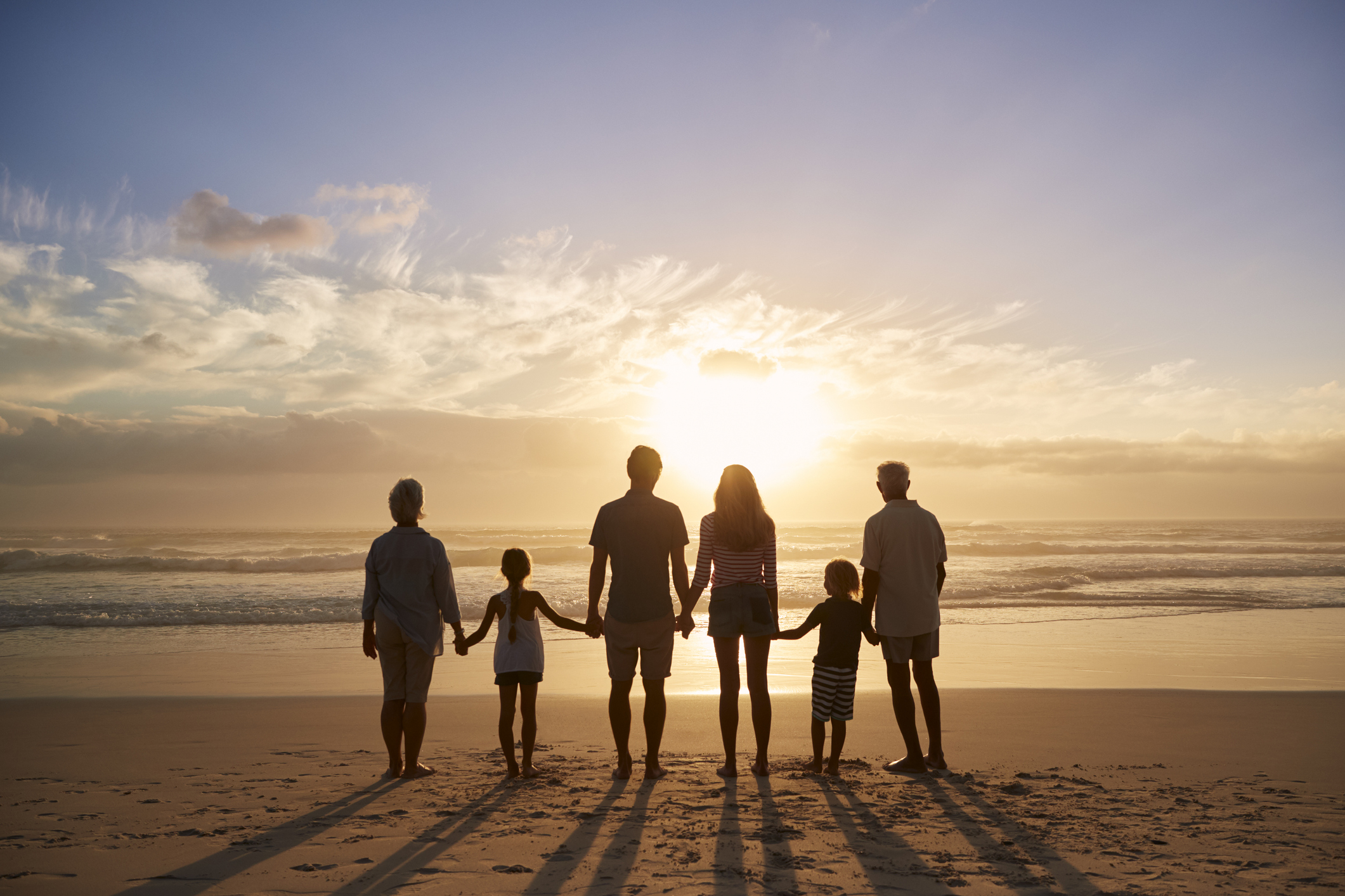 Rückansicht einer Familie mehrerer Generationen, die sich am Strand als Silhouette abzeichnet