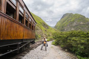 Eine ältere Dame, eine Passagierin, macht ein Foto am Bahnhof des alten Touristenzuges Nariz pdel Diablo in der Nähe von Alausi, Ecuador.