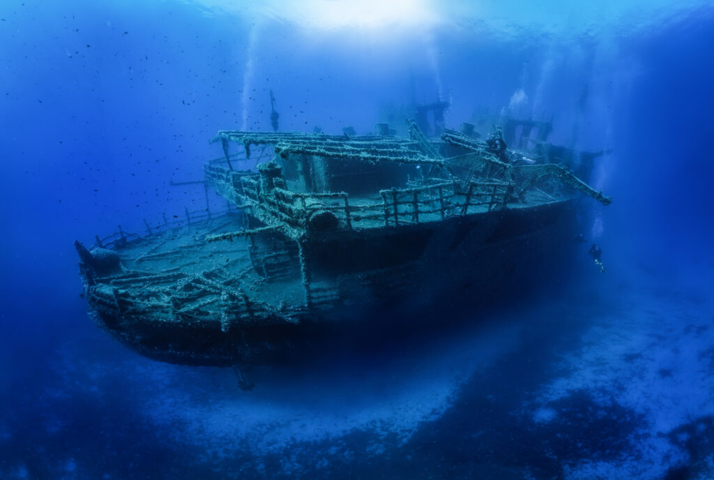 Eine Gruppe unkenntlicher Taucher erkundet ein großes, gesunkenes Schiffswrack im blauen Mittelmeer vor der Insel Naxos, Griechenland.