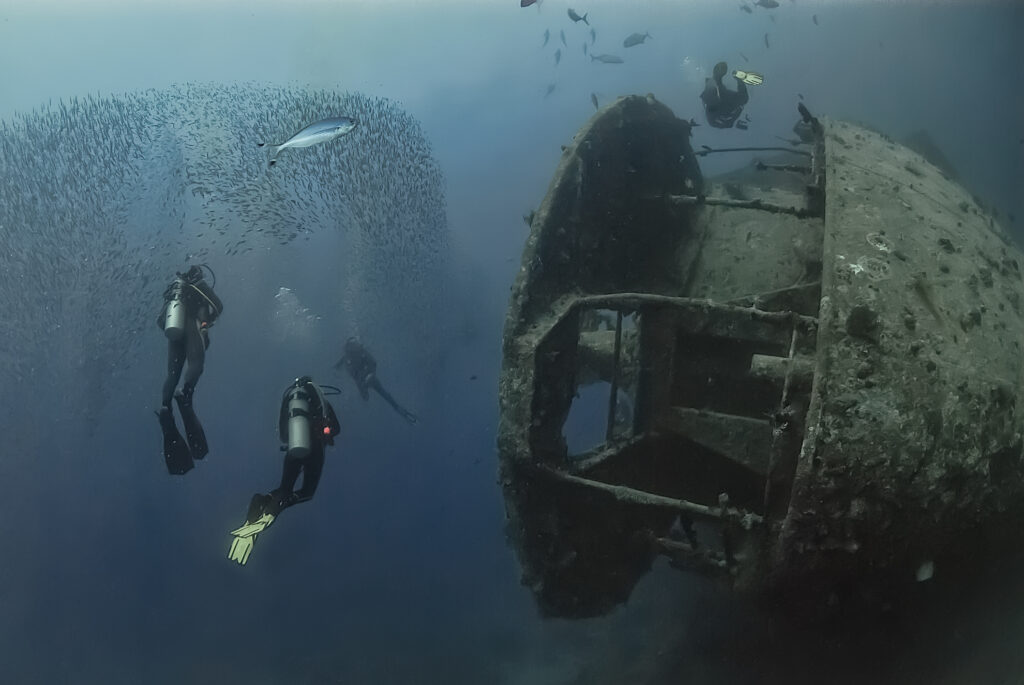 Taucher schwimmen neben dem legendären Wrack der SS Thistlegorm, einem Schiffswrack aus dem Zweiten Weltkrieg im Roten Meer, das von Meereslebewesen und historischen Geheimnissen wimmelt.