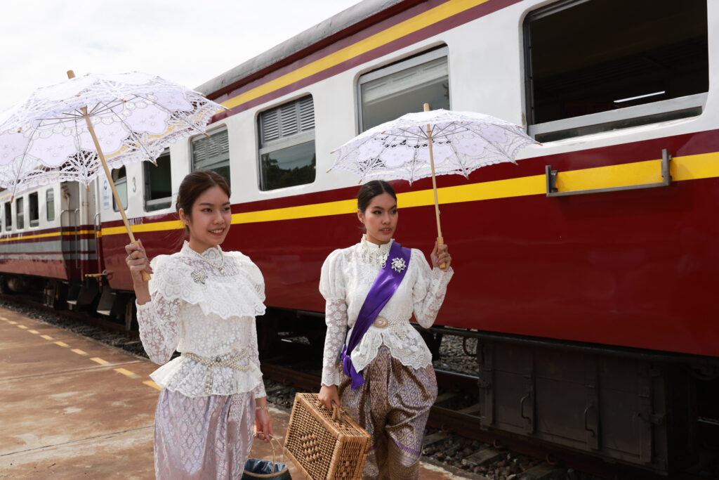 Zwei charmante Touristinnen in traditioneller thailändischer Tracht mit Retro-Schleppe vor einem Zug