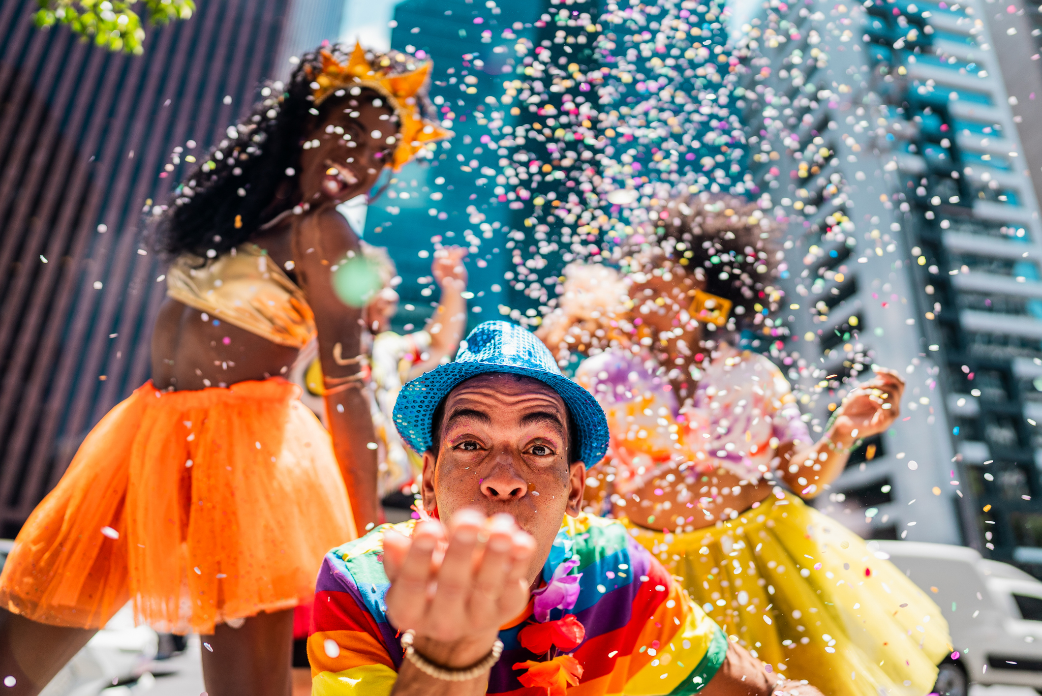 Porträt eines Mannes mittleren Alters, der Konfetti bläst und sich mit Freunden auf dem Straßenkarneval amüsiert.