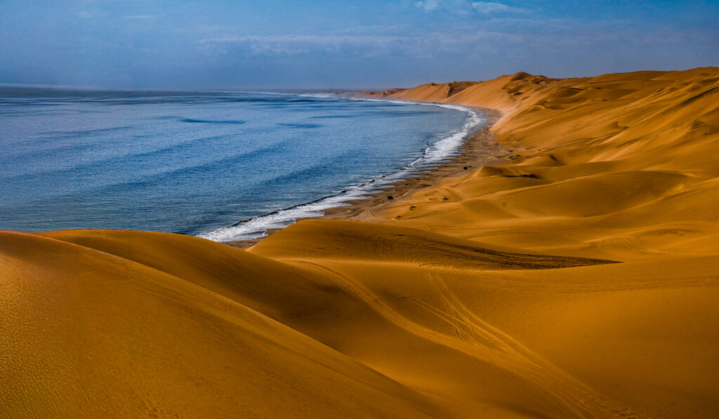 Endlose goldene Dünen der Namib-Wüste erstrecken sich südlich von Walvis Bay in Namibia direkt in den Atlantischen Ozean.