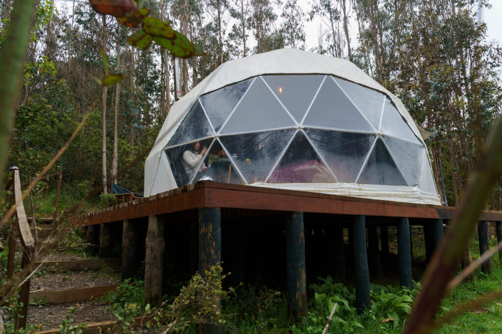 Frau und Kind entspannen sich in einer Glamping-Kuppel auf einer erhöhten Holzterrasse in einem Wald