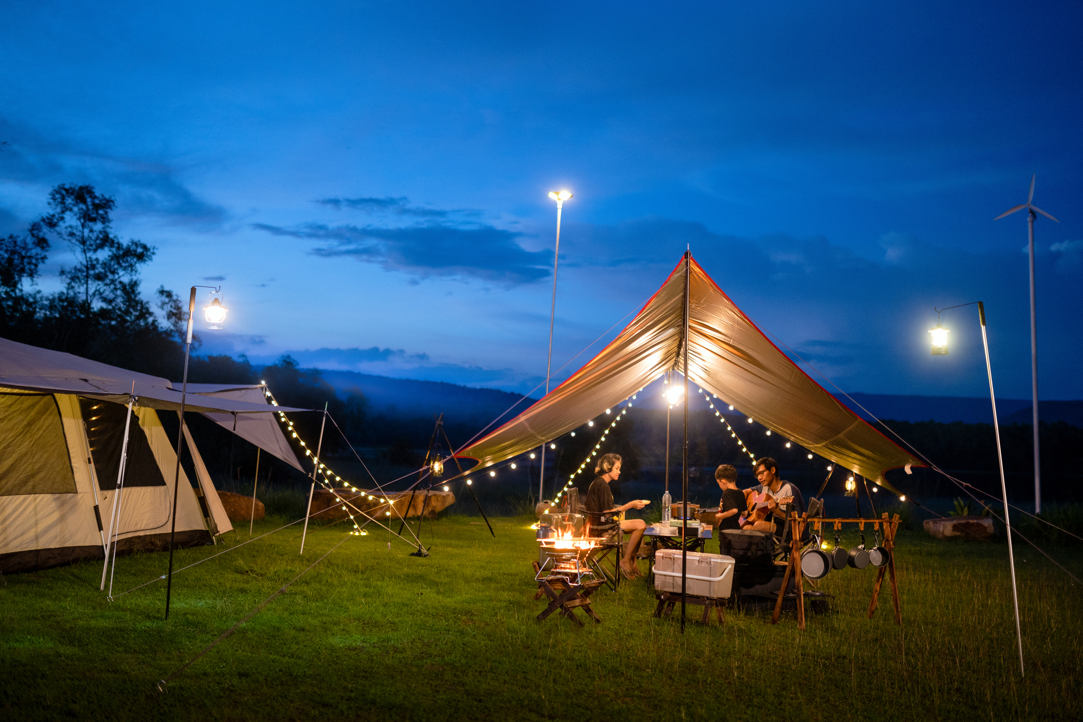 Nachtglamping mit Zeltübernachtung und Sitzgelegenheiten, eine asiatische Familie beim Abendessen, Gitarrespielen und Spaßhaben.