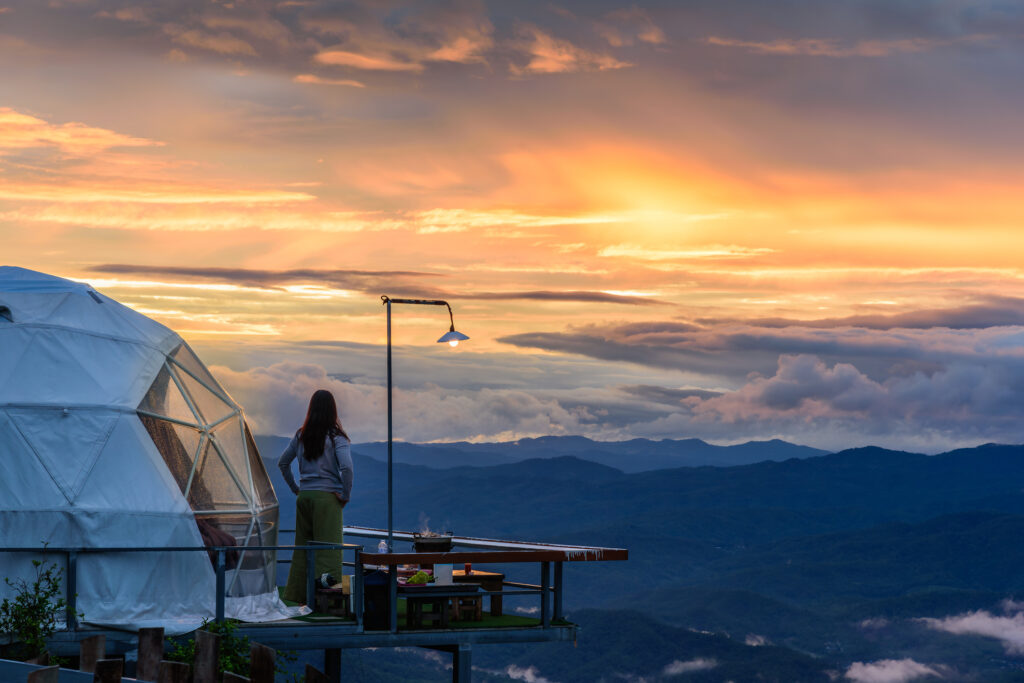 Frau genießt wunderschönen Sonnenuntergang im Glamping-Kuppelzelt mit Bergblick bei Sonnenuntergang.