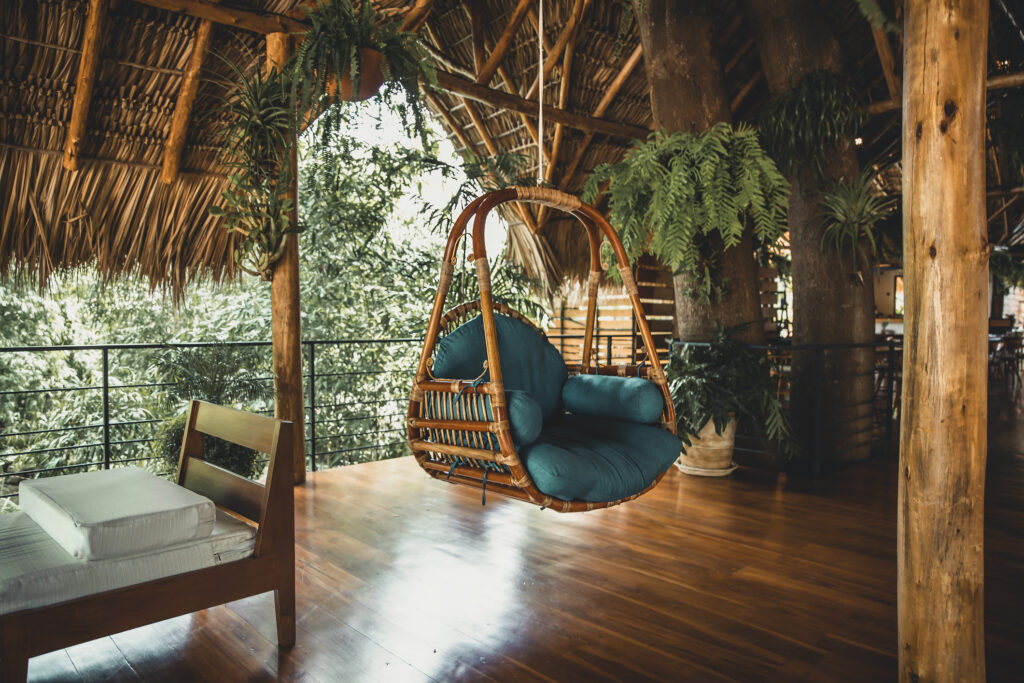 Gemütliche Veranda im Boho-Stil mit Gartenmöbeln. Frühlingsterrasse mit Pflanzen, Hängesessel und bequemem Sofa.