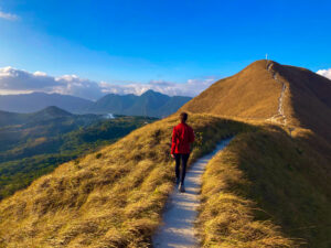 Junge Frau wandert auf einem schmalen Pfad in einem Berggebiet.