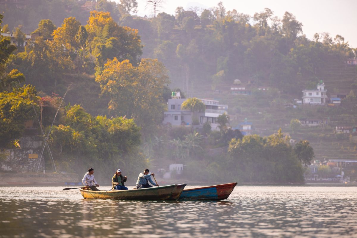 Boot auf dem stillen Phewa-See vor malerischer Uferkulisse in Pokhara, Nepal