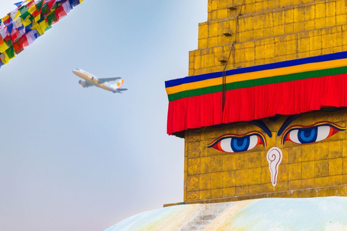 Boudhanath-Stupa mit Gebetsfahnen und Flugzeug am Himmel in Kathmandu, Nepal