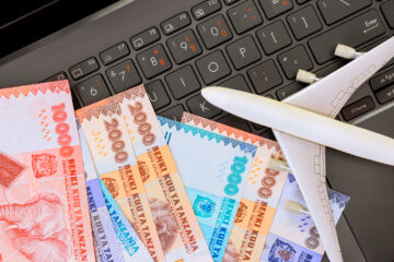 Stapel von tansanischen Schilling-Banknoten und ein Modellflugzeug liegen auf der Laptop-Tastatur und symbolisieren die Reiseplanung.