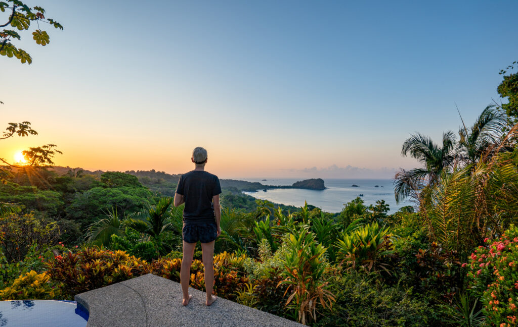 Eine Frau genießt einen strahlenden Sonnenaufgang über der wilden, ungezähmten Küstenlandschaft des Manuel-Antonio-Nationalparks an der Pazifikküste Costa Ricas.