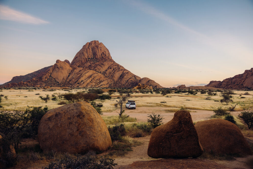 Was kostet eine Namibia Privatreise Luftbild eines Lastwagens mit Dachzelten, der im hellen Morgengrauen in Namibia, Südafrika, inmitten der majestätischen Klippen und Berge der Spitzkoppe parkt.