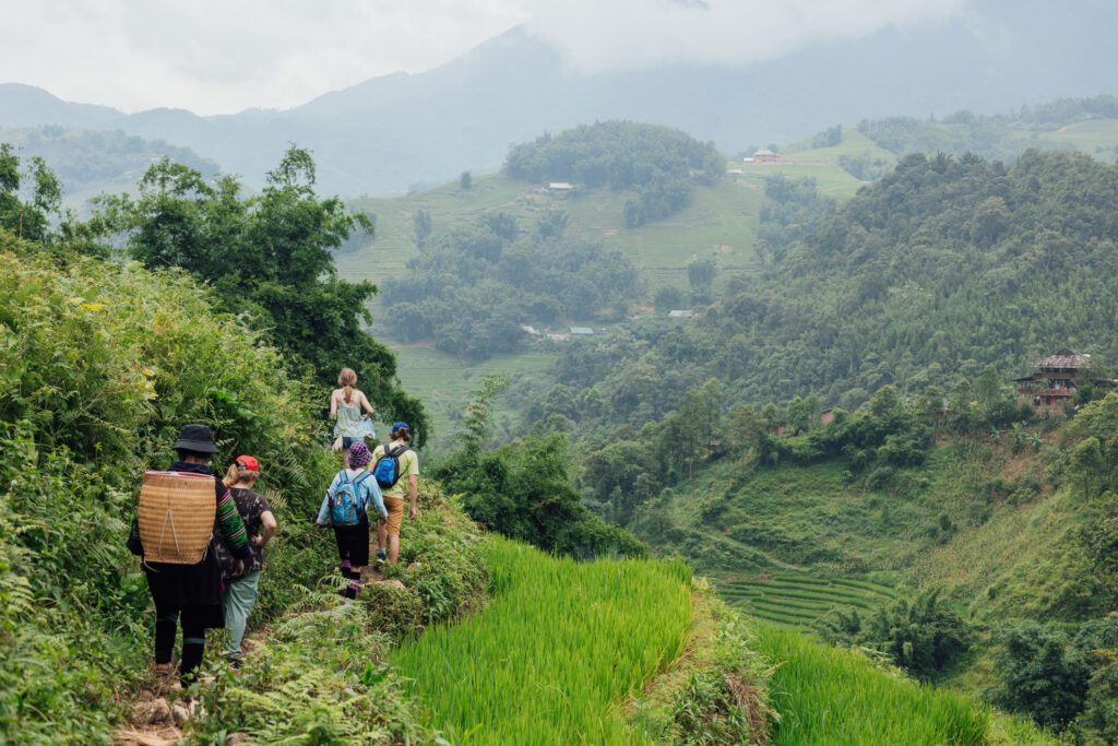 Eine Gruppe Touristen spaziert durch die Reisterrassen von Sa Pa in Vietnam. Im Hintergrund des Tals sind weitere Terrassen zu sehen.