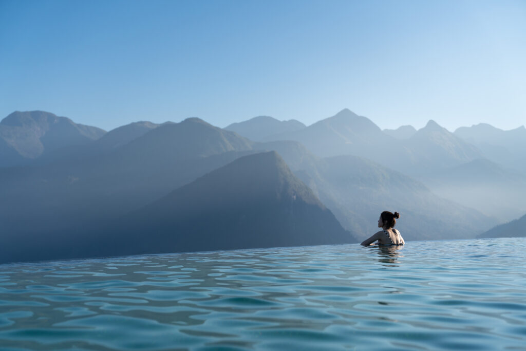 Frau entspannt sich in einem Infinity-Pool und genießt den atemberaubenden Bergblick in einem luxuriösen Resort / Urlaubskonzept