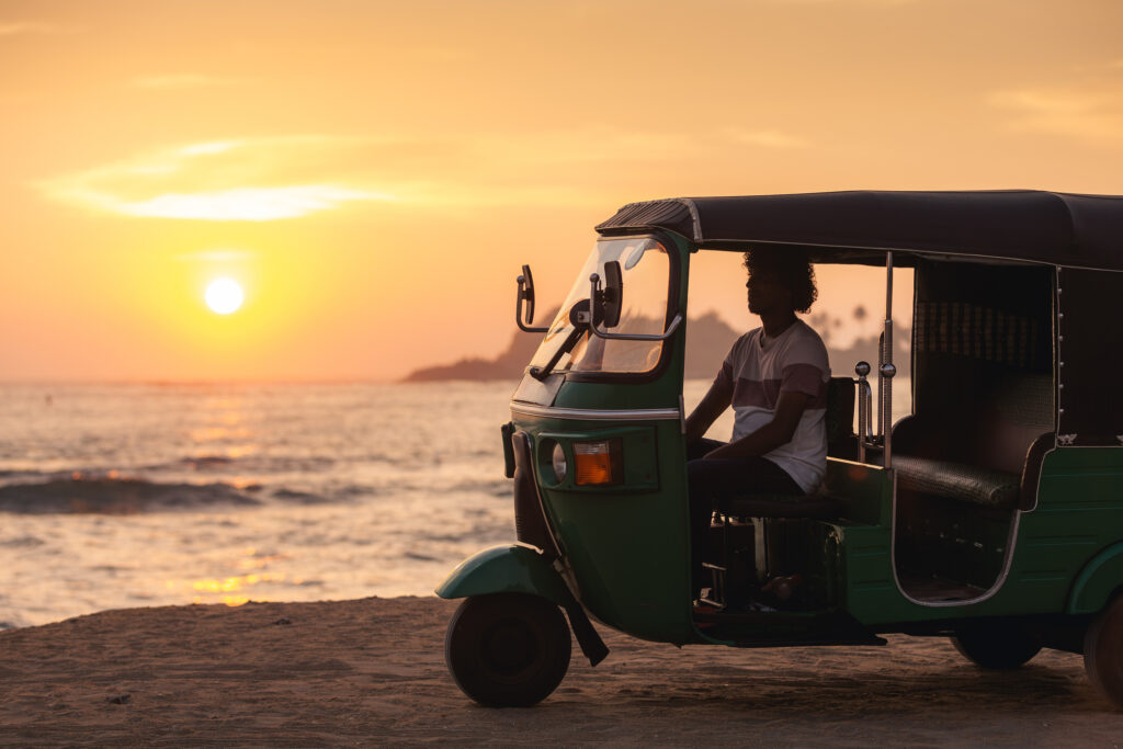 Ein Tuk-Tuk-Fahrer wartet bei Sonnenuntergang an einem Sandstrand in Sri Lanka.