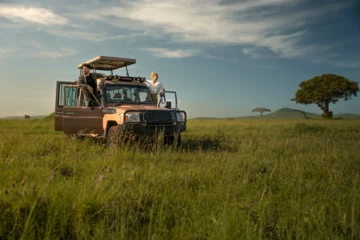 Paar an einem Safarifahrzeug in der Graslandschaft der Serengeti in Tansania
